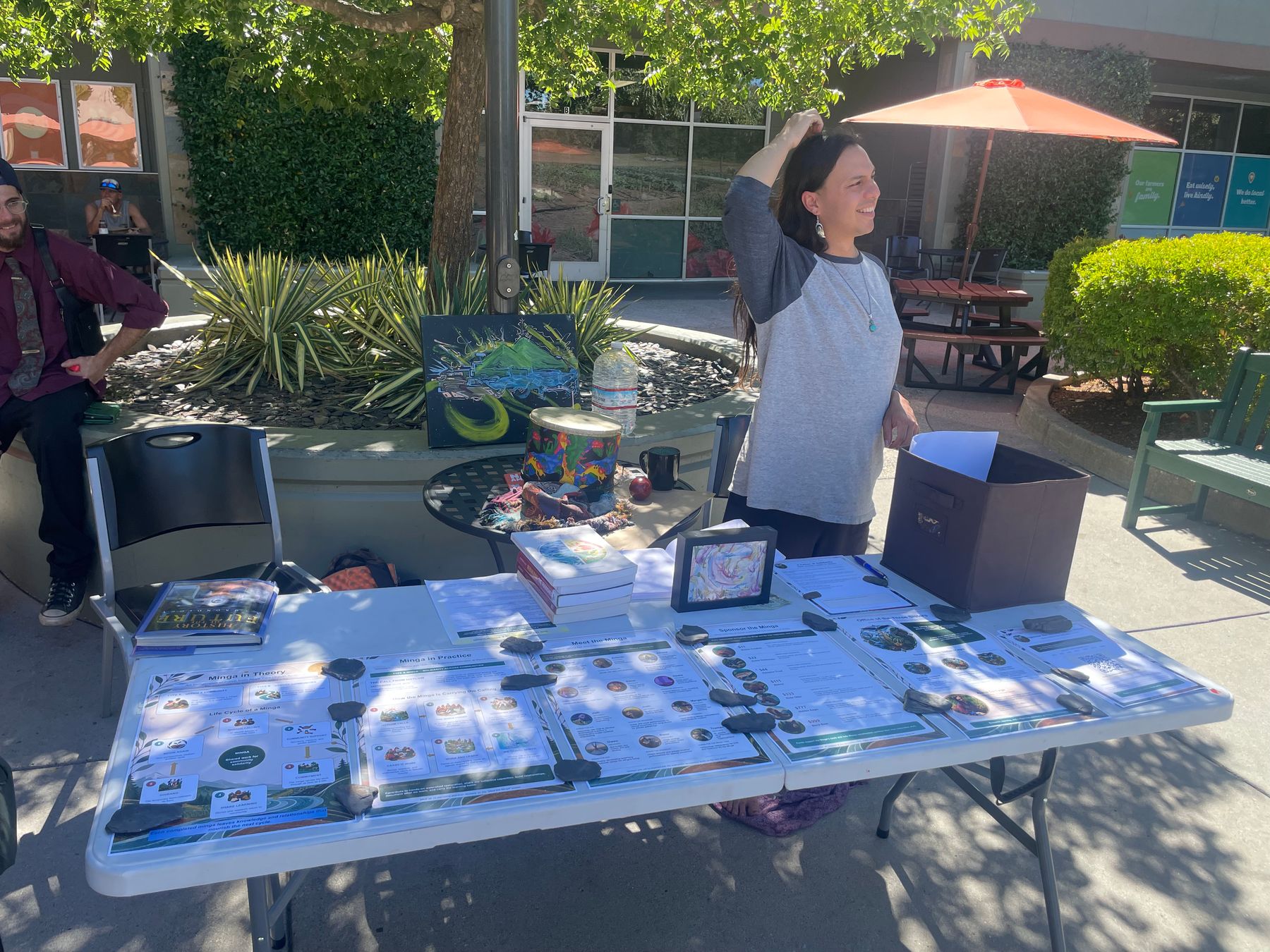 Alana detrás de una mesa con carteles de la Minga, obras de arte y libros frente a BriarPatch Co-op.